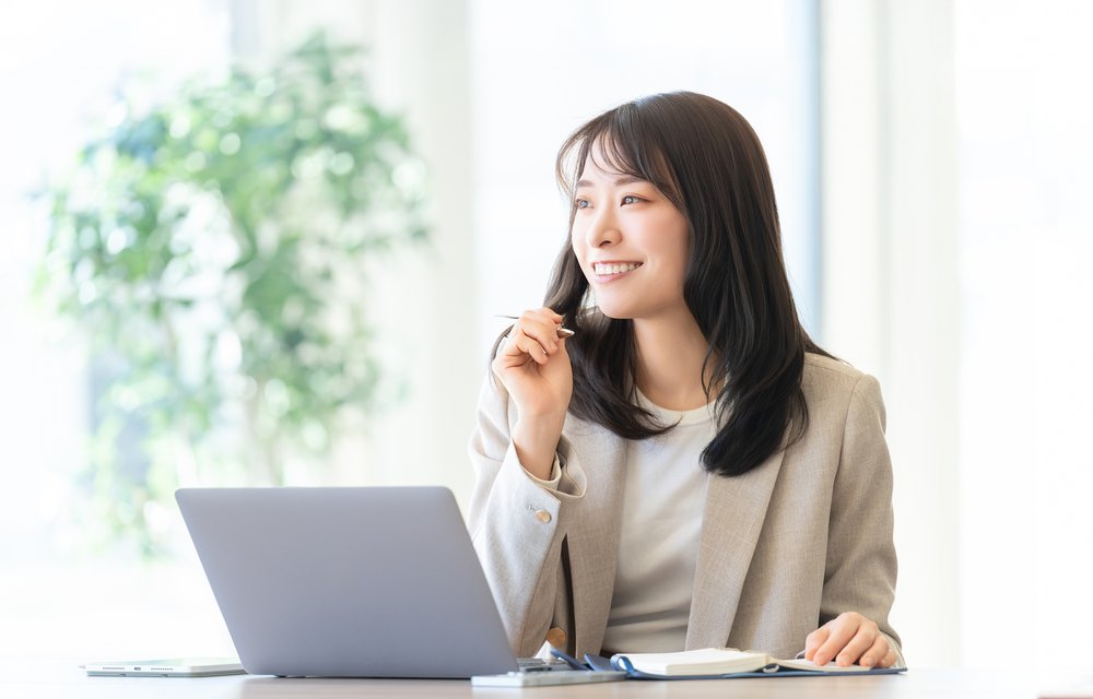 明るいオフィスでPCと手帳を前に微笑む女性